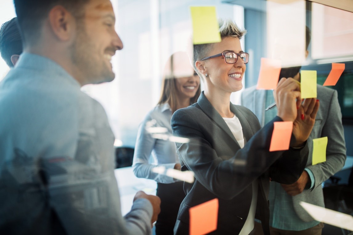 People adding post its on a glass wall of a meeting room and smiling